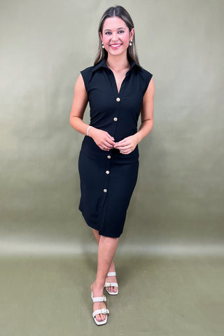 Woman wearing a black dress with white buttons against a plain background