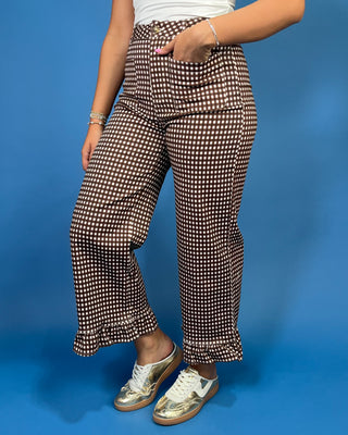 A person wearing brown and white checkered wide-leg pants with a ruffled hem, paired with white sneakers