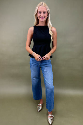 Woman wearing a black sleeveless top and blue jeans against a plain background