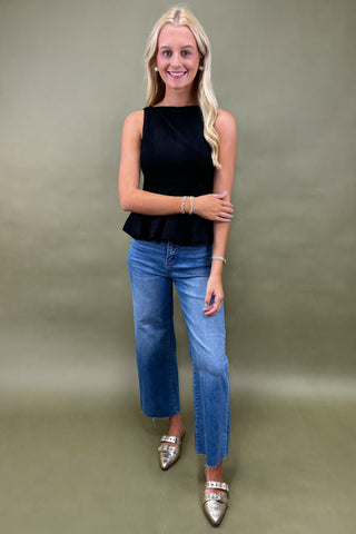 Woman wearing a black sleeveless top and blue jeans against a plain background