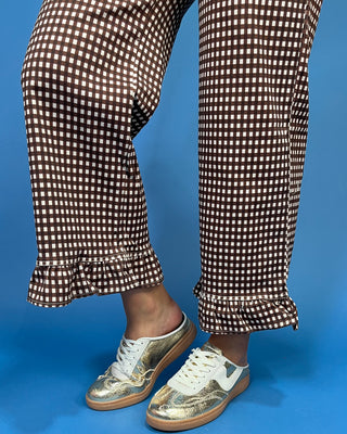 Brown and white gingham checkered pants with ruffled hems, worn with metallic gold sneakers
