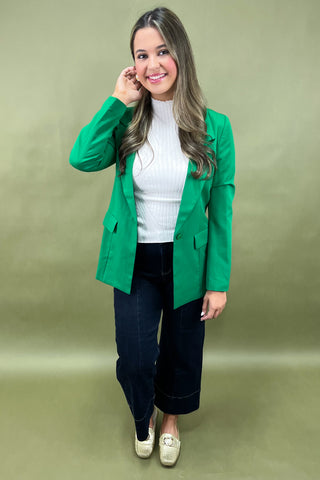 Woman wearing a green blazer over a white top and dark pants on a green background