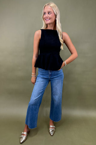 Woman wearing a black sleeveless top and blue jeans against a plain background