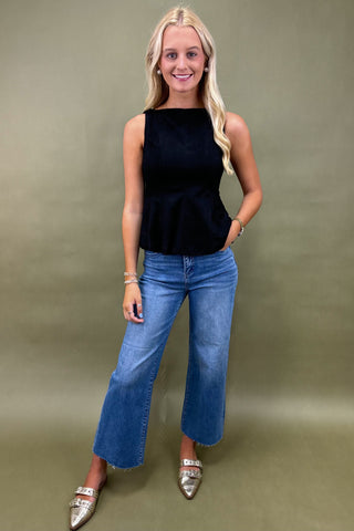 Woman wearing a black sleeveless top and blue jeans against a green background