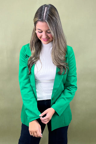 Woman wearing a green blazer over a white sweater on a beige background