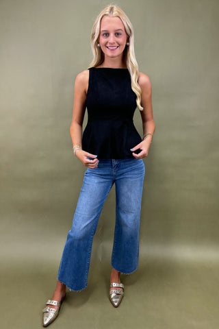 Woman wearing a black sleeveless top and blue jeans against a plain background