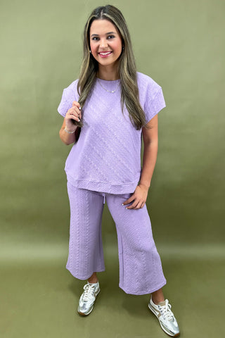 Woman wearing a purple outfit with white sneakers on a green background