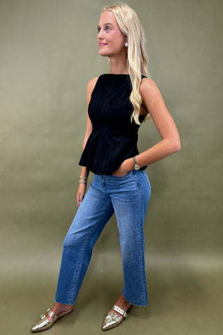 Woman wearing a black top and blue jeans against a green background