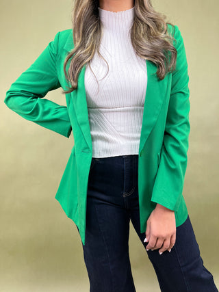 Person wearing a green blazer over a white top and dark jeans on a beige background