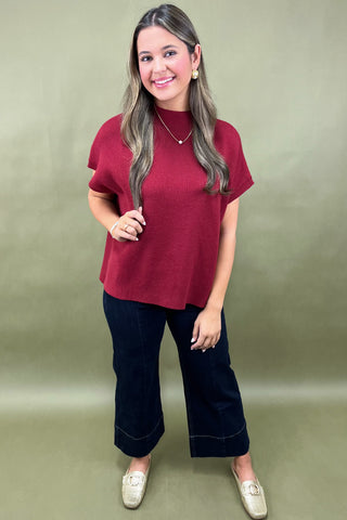 Woman wearing a red top and dark pants against a green background