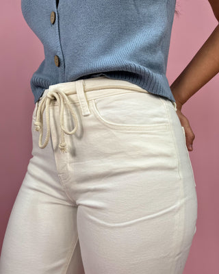 Person wearing cream-colored pants with a blue top on a pink background