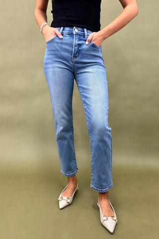 Person wearing blue jeans and white shoes on a beige background