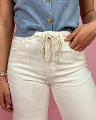 Person wearing a blue sweater and white pants against a pink background