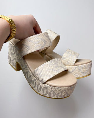 Gold platform sandal being held by a hand on a light gray background