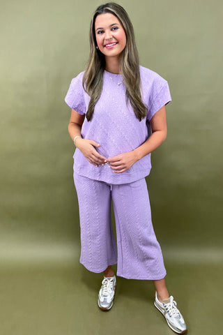 Woman wearing a purple outfit with white sneakers against a green background