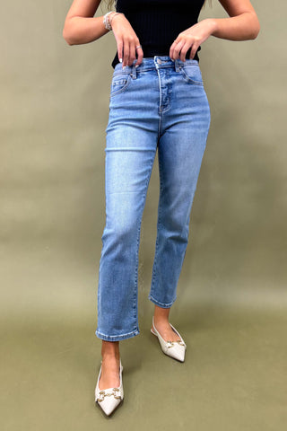 Person wearing blue jeans and white shoes on a plain background