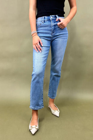 Person wearing light blue jeans and white shoes on a beige background
