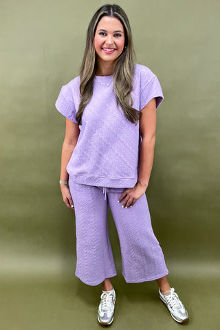 Woman wearing a purple outfit with wide-leg pants against a green background