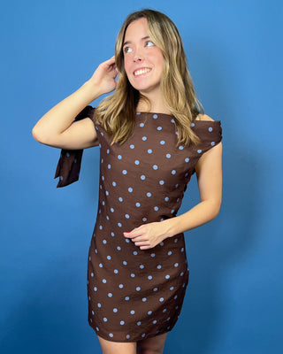 Chocolate brown mini dress with blue polka dots, off-the-shoulder neckline, and statement shoulder tie detail.