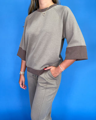 Person wearing a gray outfit with brown accents against a blue background
