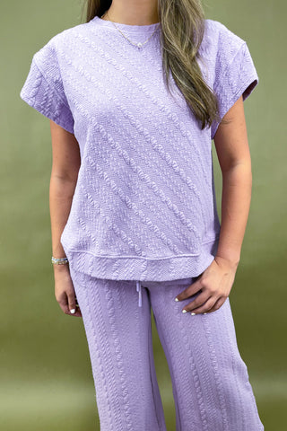 Person wearing a matching lavender top and pants set against a green background