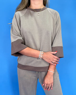 Person wearing a gray outfit with brown accents against a blue background