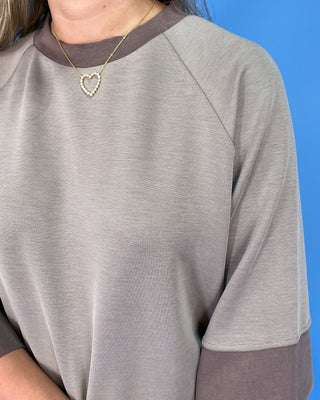 Person wearing a gray and brown long-sleeve shirt with a blue background