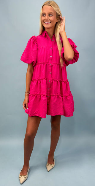 Woman wearing a bright pink dress with ruffled layers on a gray background