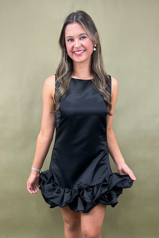 Woman wearing a black dress with ruffled hem against a beige background