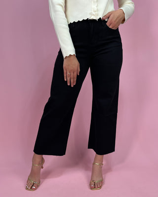 Person wearing black pants and a white top on a pink background