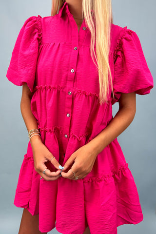 Person wearing a bright pink dress with ruffled sleeves and layers on a gray background
