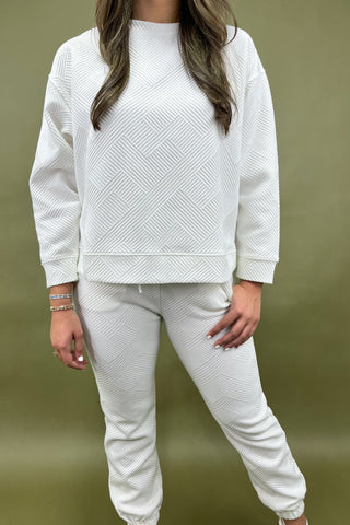 Person wearing a white textured sweatshirt and pants on a green background