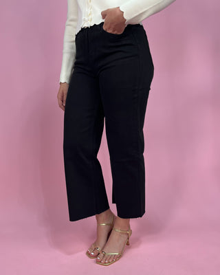 Person wearing black pants and a white top on a pink background