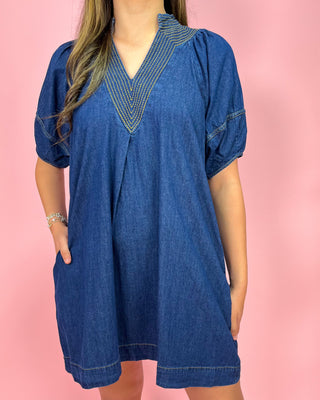 Woman wearing a blue denim dress with decorative neckline on a pink background
