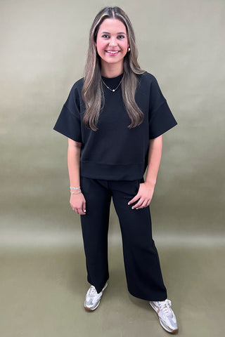 Woman wearing a black outfit with white shoes against a plain background