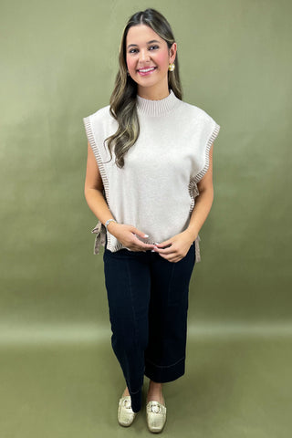 Woman wearing a white sleeveless top with fringe details on a green background
