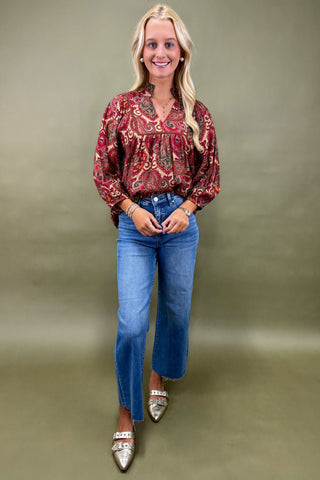 Woman wearing a patterned blouse and blue jeans against a plain background