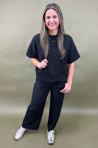 Woman wearing a black outfit with white sneakers on a plain background