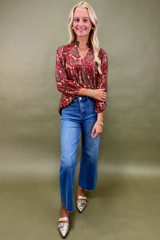 Woman wearing a red patterned blouse and blue jeans against a beige background