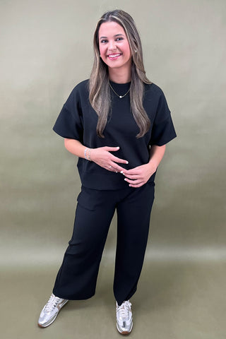 Woman wearing a black outfit with white sneakers against a beige background