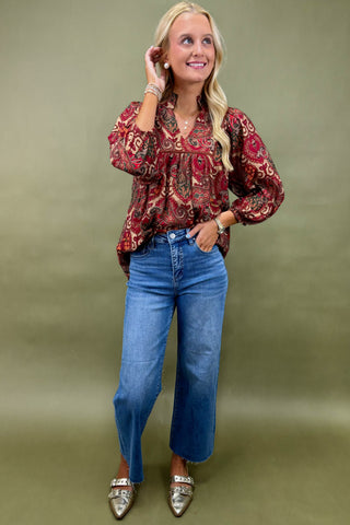 Woman wearing a patterned blouse and blue jeans against a green background