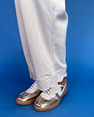 White pants with gold and white sneakers on a blue background