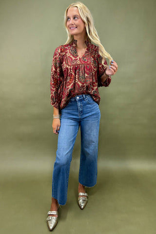 Woman wearing a patterned blouse and blue jeans against a green background