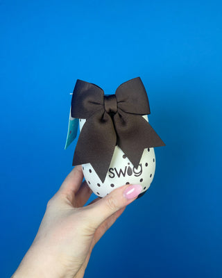 A hand holding a stainless steel travel tumbler with a brown and white polka dot pattern, set against a solid blue background.