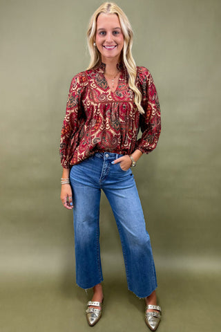 Woman wearing a patterned blouse and blue jeans against a green background