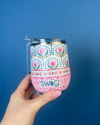 A hand holding a stainless steel travel tumbler with a multi color pattern, set against a solid blue background.