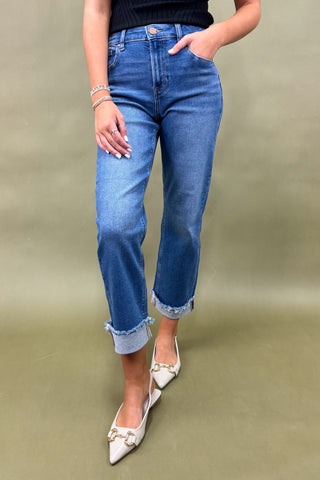 Person wearing blue jeans and white pointed-toe shoes on a plain background