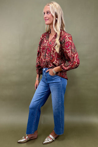 Woman wearing a patterned blouse and blue jeans against a green background