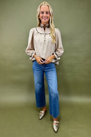 Woman wearing a beige blouse, blue jeans, and silver shoes on a green background