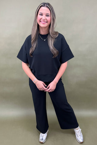 Woman wearing a black outfit with white sneakers against a plain background